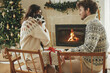 Happy young family in cozy sweaters hugging with cute cat and exchanging stylish christmas gifts on background of fireplace with modern festive mantle and christmas tree. Happy Holidays!