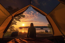 Young woman sitting in tent and looking at lake at sunset. Camping concept