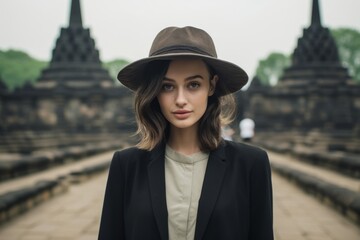 Poster - Lifestyle portrait photography of a tender girl in her 20s wearing a formal top hat at the borobudur temple in magelang indonesia. With generative AI technology