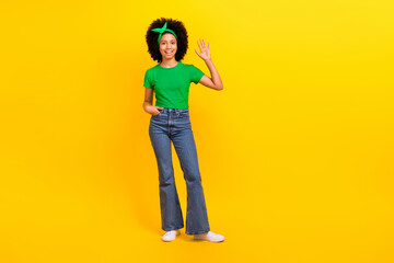 Wall Mural - Full length portrait of friendly cute cheerful girl arm palm waving hi empty space ad isolated on yellow color background