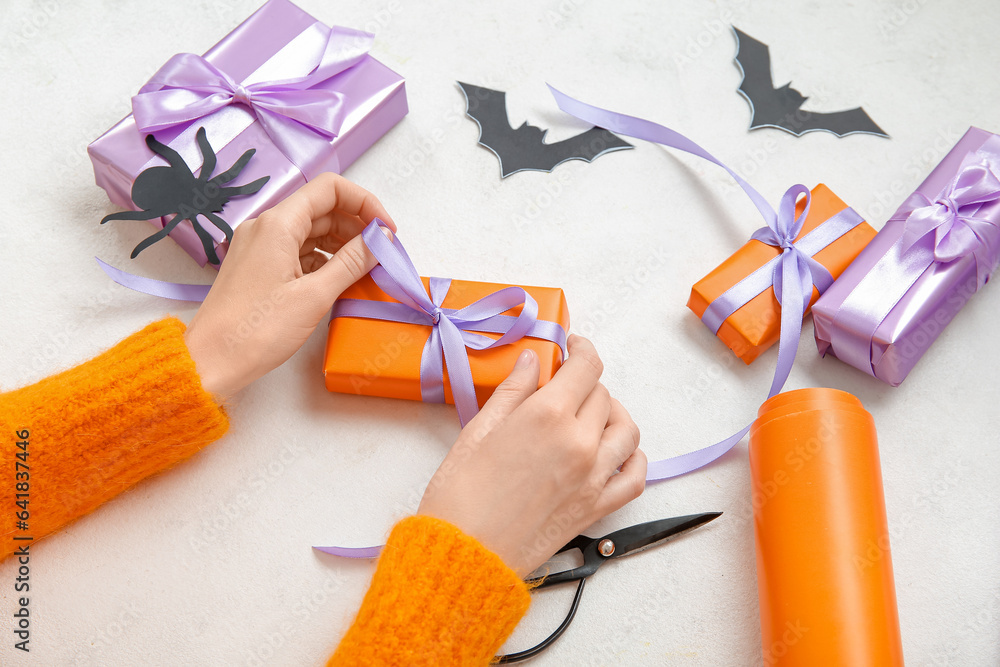 Woman tying bows on gift boxes for Halloween against white background