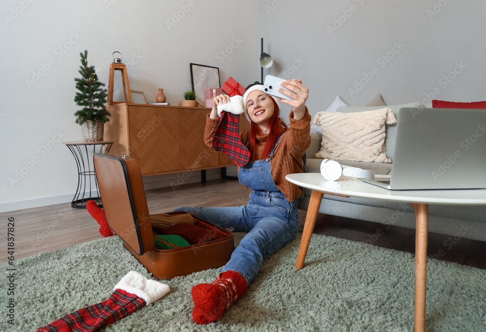 Young woman with Christmas sock taking selfie at home