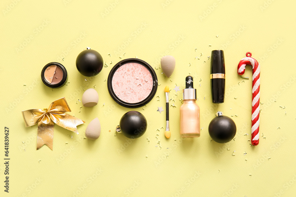 Composition with decorative cosmetics and Christmas decor on light yellow background