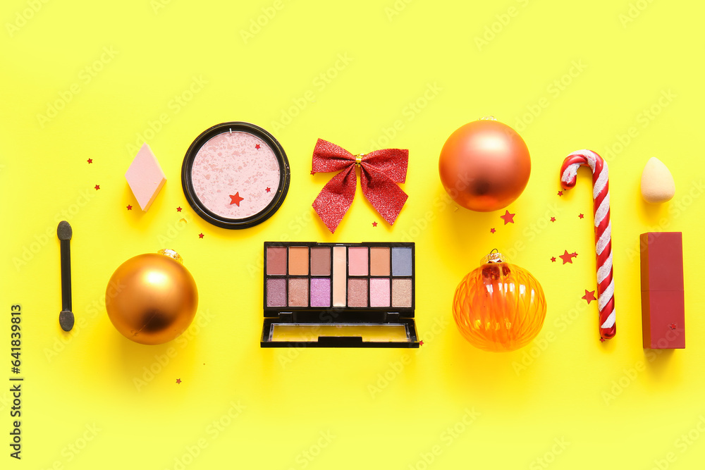 Composition with decorative cosmetics and Christmas decor on yellow background