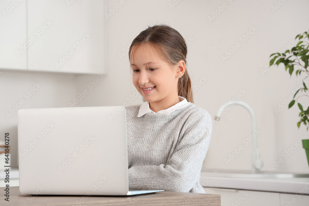 Cute little girl using laptop at table in kitchen
