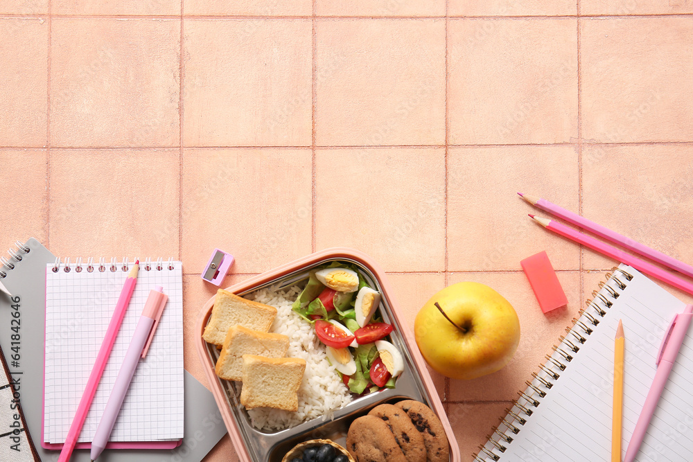 Lunchbox with delicious food and different stationery on orange tile background