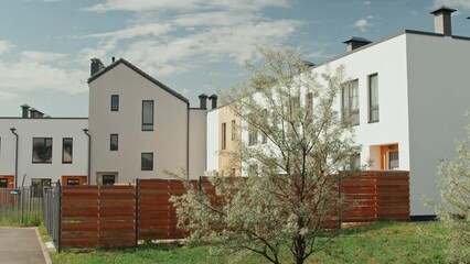 Wall Mural - Establishing panning shot of modern minimalistic two-storey apartment buildings with white walls in small town or suburban area on summer day