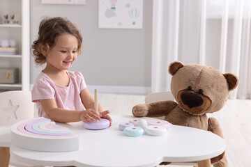 Canvas Print - Cute little girl playing with toy and teddy bear at white table in room