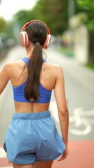 Wall Mural - Amidst the urban landscape, a girl in sportswear and headphones is doing her morning run.