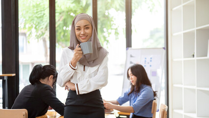 Wall Mural - A confident Muslim businesswoman stands in front of the meeting with a coffee cup in her hand