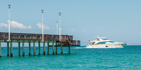 A yacht sailing near a dock on El Coromuel Beach, under a blue and sunny sky in the beautiful bay of La Paz Baja California Sur. Mexico