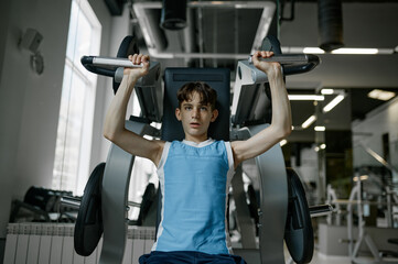 Teenager boy training arms, chest, shoulders and back on exercise machine