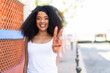 © luismolinero - Young African American woman at outdoors smiling and showing victory sign