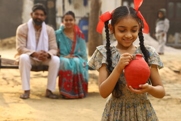 Happy rural Indian family sitting together, daughter is holding a piggy bank in her hand, putting a coin in it, showing the concept of saving money