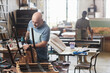© Seventyfour - Portrait of senior craftsman in furniture restoration workshop fixing old wooden chair, copy space