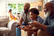 © Monkey Business - Multi-Generation Male Family Sitting On Sofa At Home Playing Video Game Together