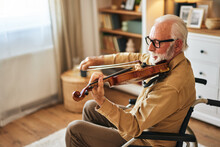Elderly Man In The Wheelchair Playing The Violin At Home