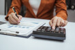 © R Photography - Close up hands of woman in brown formal suit checking bills, taxes, bank account balance, using calculator, Personal Checking, Empower Checking, Personal Savings, Certificates, IRAs, Money Market