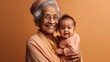 © iuricazac - A joyful senior grandmother holds her grandkid in a beige background. Generative AI