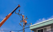 Two electricians with crane truck are installing electrical equipment on electric power pole against blue sky background