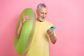 Wall Mural - Portrait of positive retired person with white hair hold inflatable ring look at smartphone read post isolated on pink color background