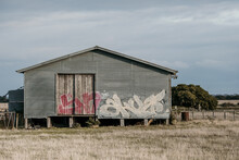 Rural Shed With Graffiti On Grassy Landscape