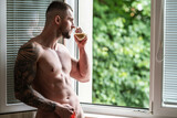Handsome muscular man drink coffee in bedroom on window curtains. Young handsome sexy man resting at home. Guy with athletic muscles. Sexy young handsome naked man on bedroom. Seductive gay.