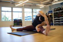 Physically fit woman stretching before exercise in a gym. She is exercising on a yoga mat. 
