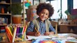 young African-American artist, an enthusiastic little boy, sits on a table and immerses himself in creating a colorful masterpiece on a book using markers.