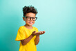 © deagreez - Portrait of cute small boy with brown hair wear stylish t-shirt in glasses hold product empty space isolated on teal color background