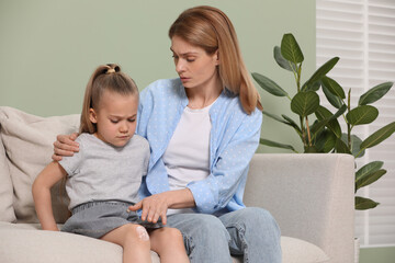 Wall Mural - Mother applying ointment onto her daughter's knee on couch indoors