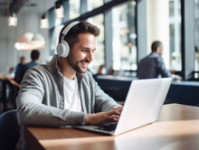 Smiling male office worker wearing headphones in front of laptop working and making a video call