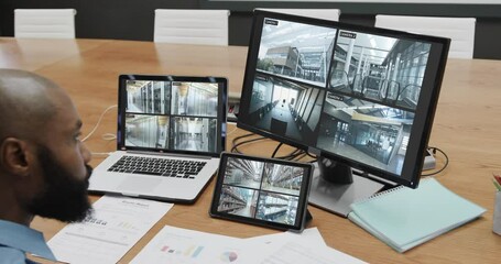 Poster - African american male security officer watching cctv camera views on computer screens, slow motion