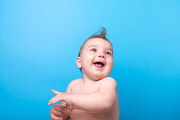 Wall Mural - A nine-month-old baby on a blue background. Looks, emotional, funny, copy space.