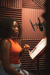 © ADDICTIVE STOCK - Focused black female standing and recording song near microphone equipment in studio