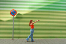 Young Woman Pointing Away Against Green Wall
