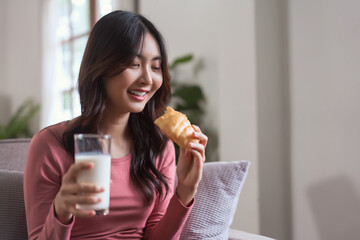 Women leisure on sofa to drinking milk and eating bread with healthy meal in lifestyle at home.