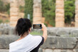 Woman taking a photo at the sanctuary of Apollo at Delphi in Greece. A famous touristic destination.
