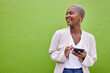 © Chanelle Malambo/peopleimages.com - Woman, thinking and phone for communication by a wall or green background with internet. Happy African female person outdoor with a smartphone for social media, networking app and chat mockup space