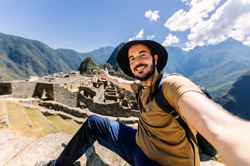 Happy young adult man taking selfie portrait in Machu Picchu. Joyful traveler enjoying vacation visiting Peru. South american travel holidays concept.