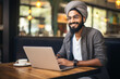 Smiling handsome hipster Indian man sitting and working on his laptop in coffee shop in Paris