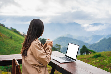 Young woman freelancer traveler working online using laptop and enjoying the beautiful nature landscape with mountain view