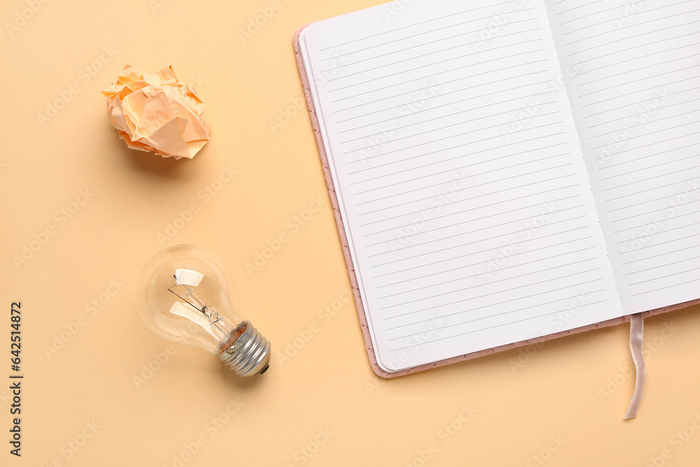 Notebook with light bulb and crumpled paper on beige background. Logic concept