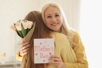 Canvas Print - Mature woman with tulips and card for Mother's Day hugging her daughter at home