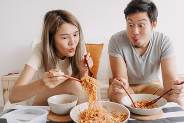 Funny asian couple lover eating quick noodle together.