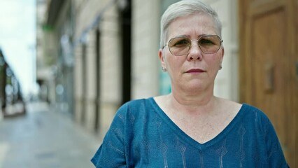 Wall Mural - Middle age grey-haired woman standing with serious expression at street