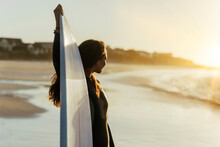 Young Beautiful Female Surfer On A Sandy Beach Getting Ready To Surf During A Beautiful Sunset