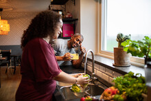 Interracial middle aged couple taking a photo with a smart phone while preparing a healthy dish with fresh fruits and vegetables at home representing a healthy lifestyle and diet