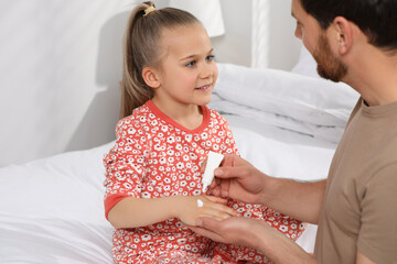 Wall Mural - Father applying ointment onto her daughter's hand on bed