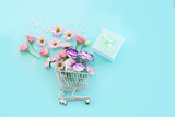 Fototapeta Mapy - Shopping cart with flowers and gift box over pastel blue background. Holidays shopping and sale concept